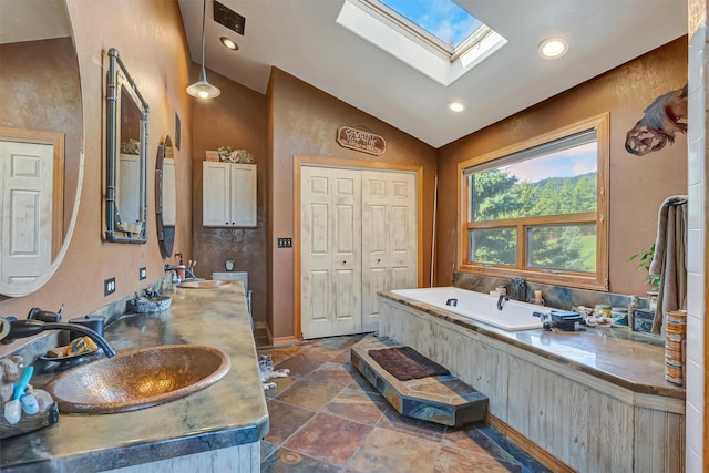 bathroom with lofted ceiling, a skylight, a bath, double vanity, and recessed lighting