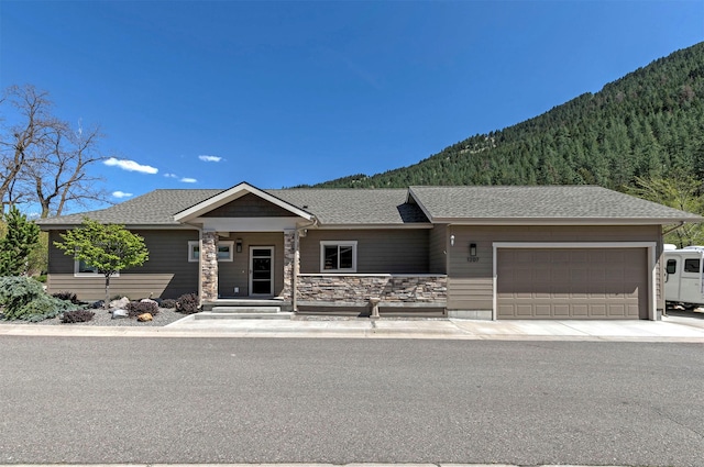 single story home with stone siding, a garage, a shingled roof, and a mountain view