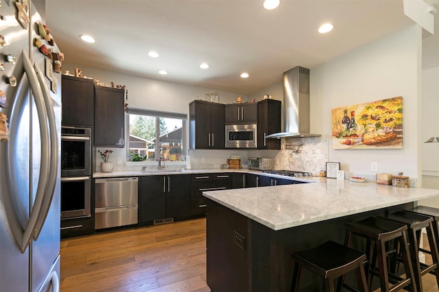 kitchen with a peninsula, a kitchen bar, stainless steel appliances, visible vents, and wall chimney range hood