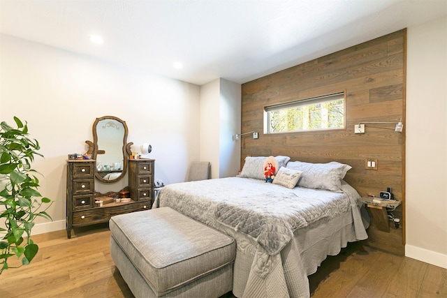bedroom featuring light wood finished floors, wooden walls, baseboards, and recessed lighting