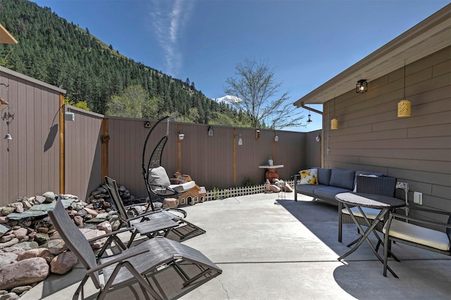 view of patio featuring an outdoor hangout area, a forest view, a mountain view, and a fenced backyard