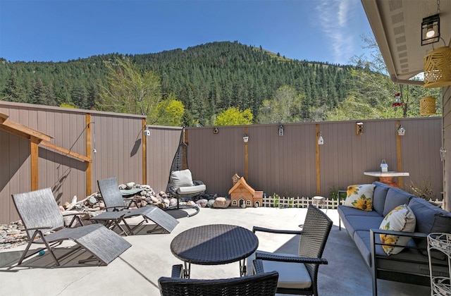 view of patio featuring a fenced backyard, a wooded view, an outdoor living space, and a mountain view