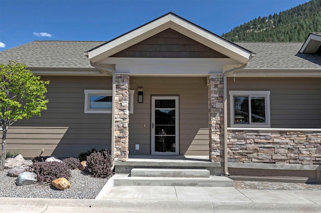 entrance to property with a mountain view, a shingled roof, and stone siding