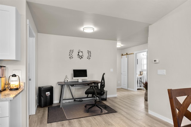 office space featuring baseboards, light wood-style flooring, and a barn door