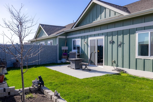 rear view of house with fence, a lawn, a shingled roof, board and batten siding, and a patio area