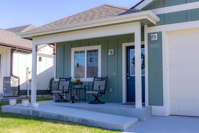 doorway to property featuring covered porch, roof with shingles, a garage, and board and batten siding