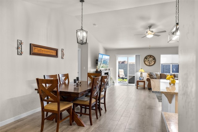 dining space featuring ceiling fan with notable chandelier, baseboards, and wood finished floors