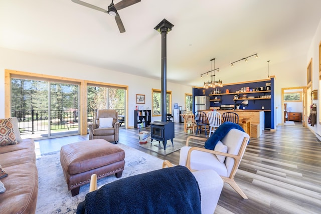 living area featuring a ceiling fan, track lighting, indoor bar, wood finished floors, and a wood stove