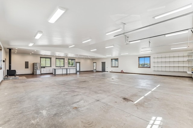 garage with electric panel, a wood stove, and stainless steel refrigerator with ice dispenser