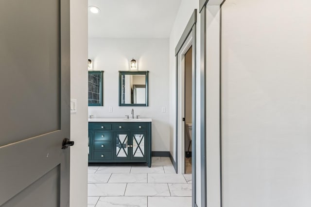 bathroom with a sink, toilet, marble finish floor, double vanity, and baseboards