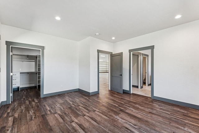 unfurnished bedroom with baseboards, a walk in closet, and dark wood-type flooring