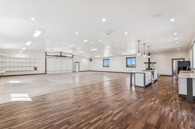 interior space featuring hanging light fixtures, a sink, open floor plan, wood finished floors, and an island with sink