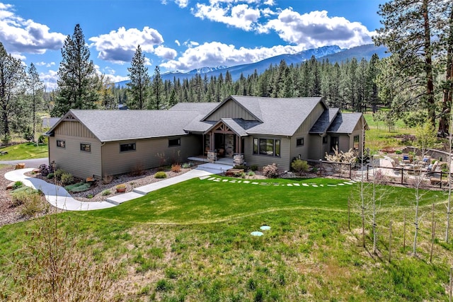 ranch-style home featuring a mountain view, board and batten siding, a shingled roof, and a front lawn