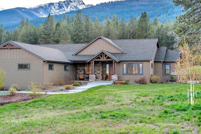 view of front facade with board and batten siding, a wooded view, a front yard, and a mountain view