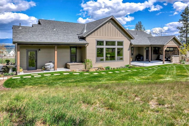 back of property with a yard, a patio area, a shingled roof, and board and batten siding