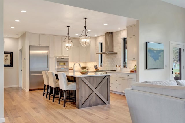kitchen with wall chimney exhaust hood, decorative backsplash, appliances with stainless steel finishes, and light wood-type flooring