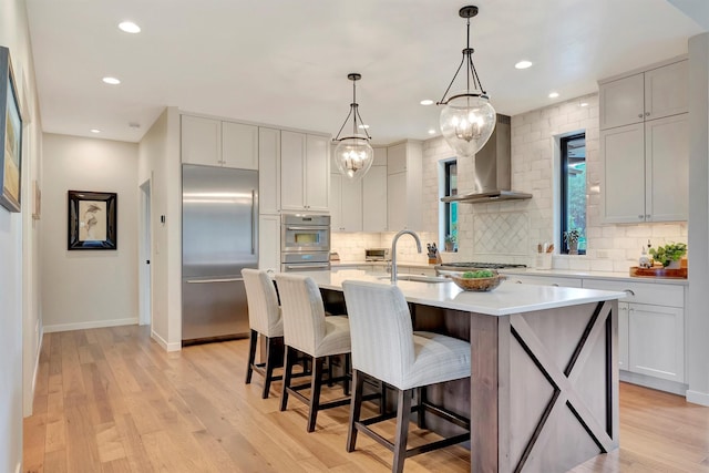kitchen with wall chimney range hood, stainless steel appliances, decorative backsplash, and a sink