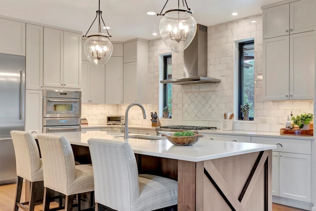 kitchen featuring wall chimney exhaust hood, stainless steel appliances, decorative backsplash, and a sink