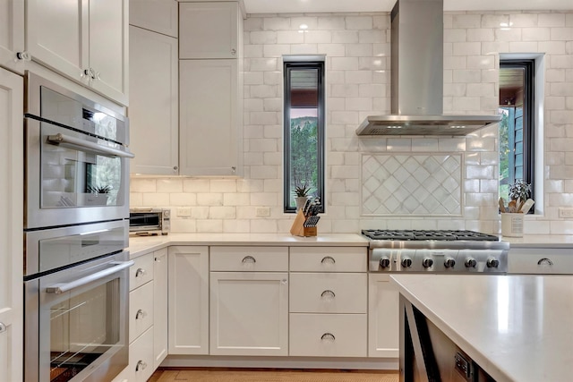 kitchen with light countertops, wall chimney exhaust hood, stainless steel appliances, and backsplash
