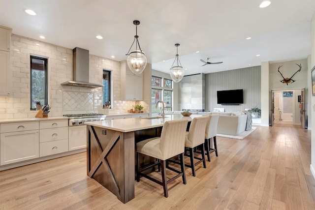 kitchen featuring a sink, stainless steel gas cooktop, a center island with sink, wall chimney exhaust hood, and light countertops