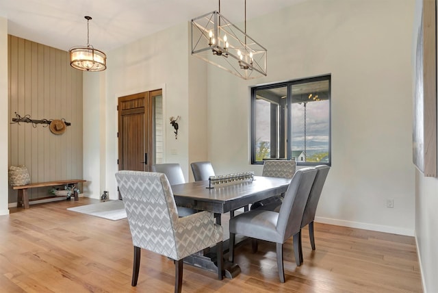 dining room featuring an inviting chandelier, light wood-style flooring, baseboards, and a towering ceiling
