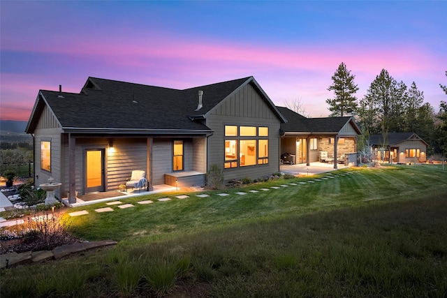 rear view of house featuring a lawn, a patio area, a shingled roof, and board and batten siding