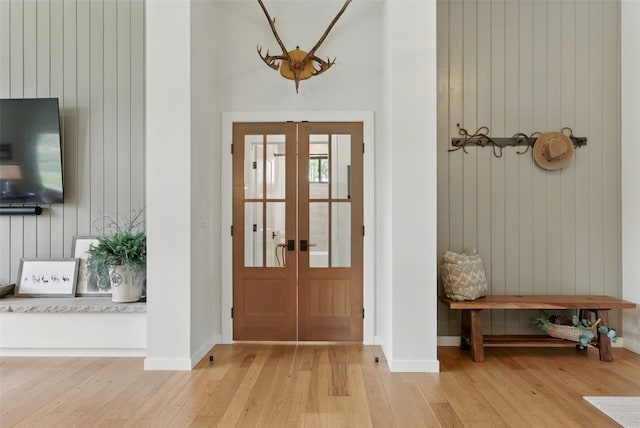doorway to outside with french doors, light wood finished floors, wood walls, a high ceiling, and baseboards