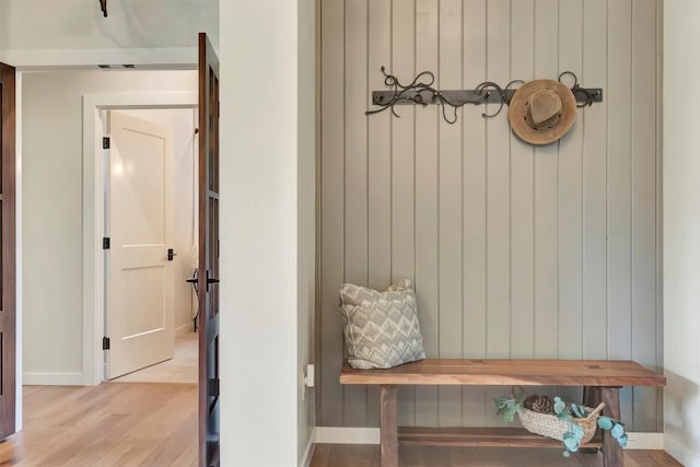 mudroom featuring light wood-type flooring, wood walls, and baseboards