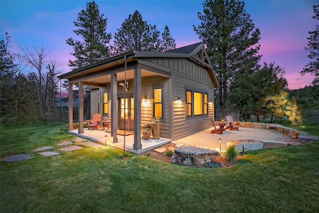 back of house featuring board and batten siding, a lawn, a patio area, and french doors