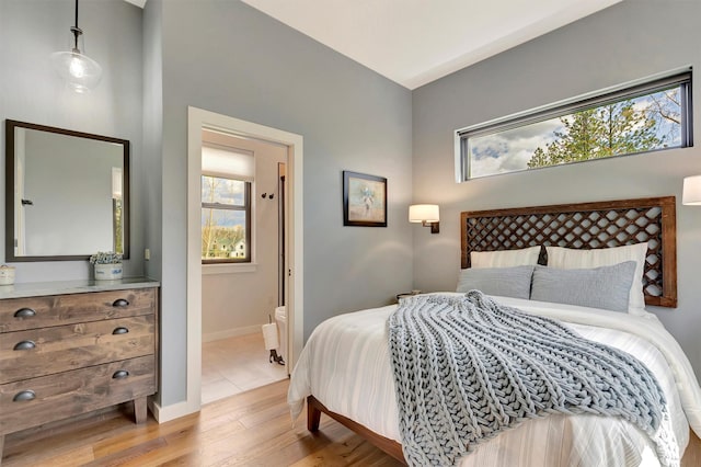bedroom with light wood finished floors, ensuite bathroom, and baseboards