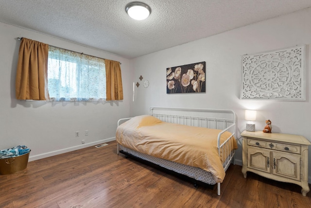 bedroom with dark wood-style flooring, a textured ceiling, baseboards, and visible vents