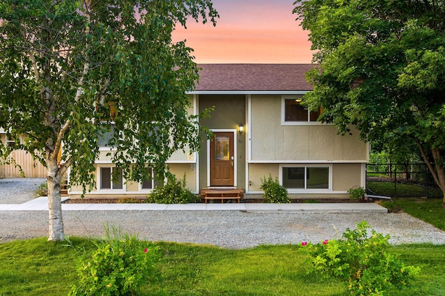 bi-level home featuring a shingled roof and fence