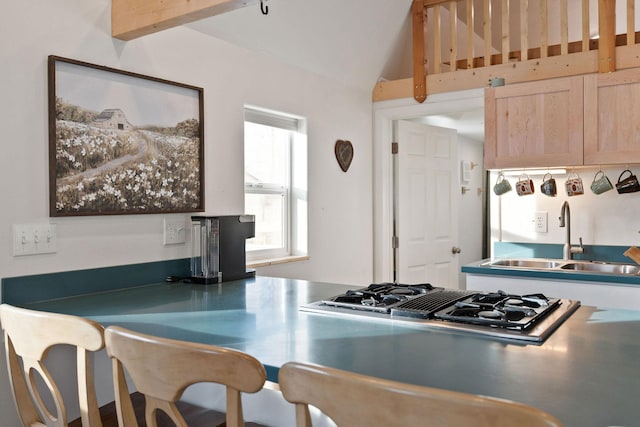 kitchen featuring stovetop with downdraft, light brown cabinets, a sink, and vaulted ceiling