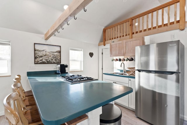 kitchen featuring a sink, lofted ceiling with beams, a breakfast bar area, light wood finished floors, and appliances with stainless steel finishes