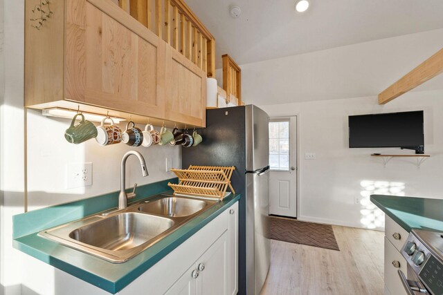 kitchen with appliances with stainless steel finishes, baseboards, a sink, dark countertops, and light wood-type flooring