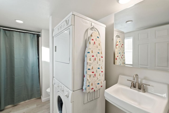 bathroom featuring toilet, wood finished floors, a sink, and stacked washer and dryer