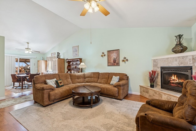 living room with a ceiling fan, lofted ceiling, a fireplace, and wood finished floors