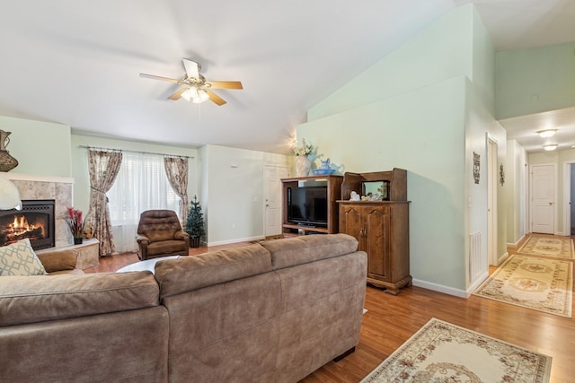 living room featuring wood finished floors, vaulted ceiling, ceiling fan, baseboards, and a tile fireplace