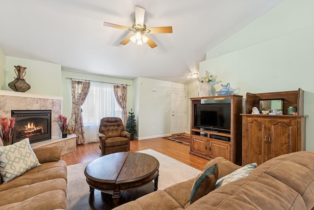 living area with a tile fireplace, light wood-type flooring, baseboards, ceiling fan, and vaulted ceiling