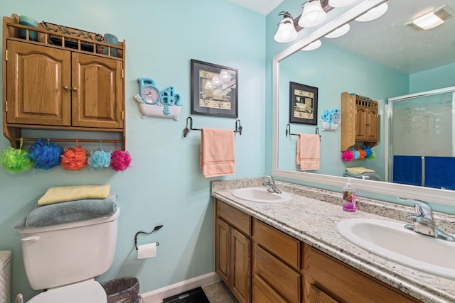 bathroom with a stall shower, toilet, double vanity, and a sink