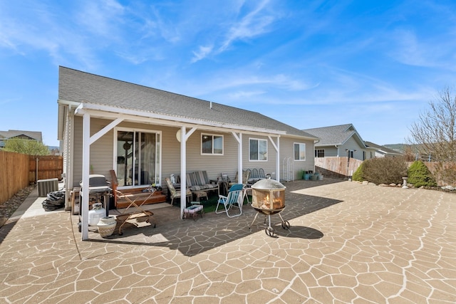 rear view of house with a patio area, roof with shingles, central AC unit, and a fenced backyard