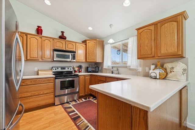 kitchen with lofted ceiling, a peninsula, light wood-style floors, light countertops, and appliances with stainless steel finishes