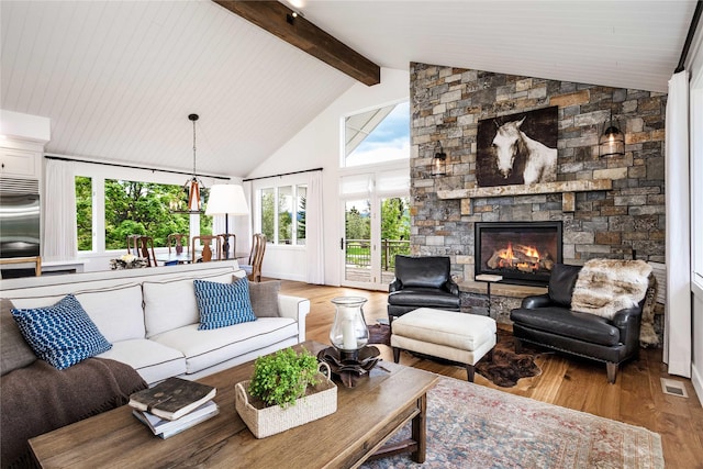 living room with visible vents, wood finished floors, a stone fireplace, and high vaulted ceiling