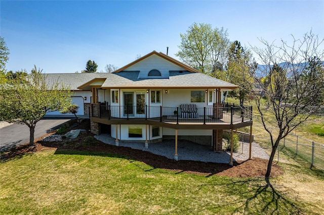 rear view of house featuring a yard, a deck, a shingled roof, and fence