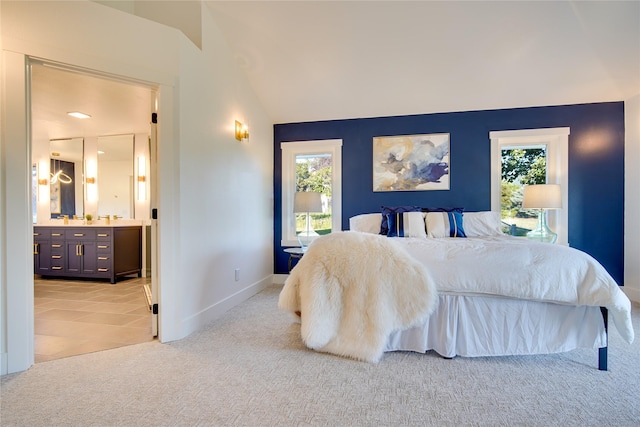 bedroom with baseboards, ensuite bathroom, light colored carpet, and vaulted ceiling