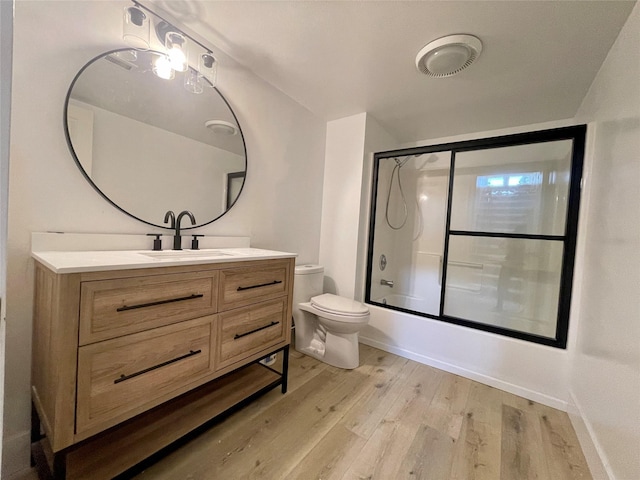 bathroom featuring toilet, wood finished floors, vanity, combined bath / shower with glass door, and baseboards