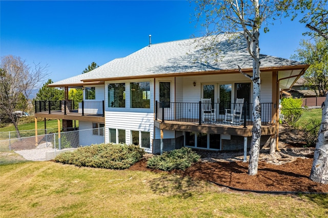 rear view of house with a balcony, a yard, a shingled roof, and fence