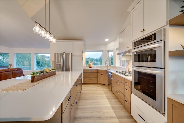 kitchen featuring light wood finished floors, a sink, stainless steel appliances, white cabinets, and decorative light fixtures