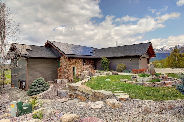view of front of property featuring stone siding, roof mounted solar panels, concrete driveway, a shingled roof, and a front yard