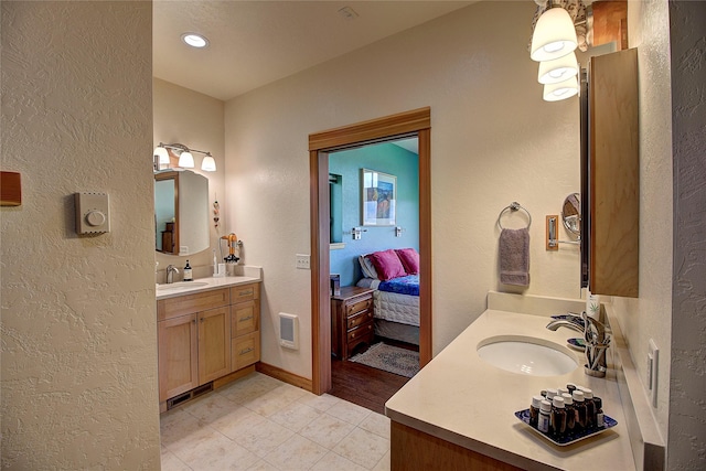 ensuite bathroom featuring tile patterned floors, a textured wall, two vanities, and a sink